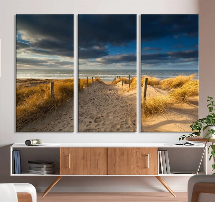 The Ocean Beach Dark Clouds Wall Art Canvas Print is a breathtaking triptych depicting a sandy beach path with tall grasses under an intense cloudy sky. It is crafted on museum-quality canvas with UV protection.