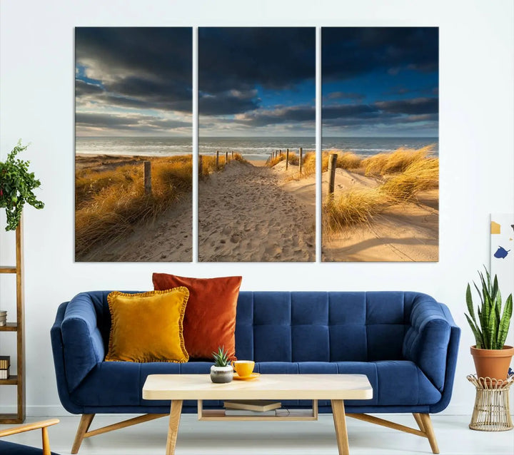 The Ocean Beach Dark Clouds Wall Art Canvas Print is a breathtaking triptych depicting a sandy beach path with tall grasses under an intense cloudy sky. It is crafted on museum-quality canvas with UV protection.