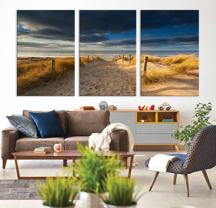 The Ocean Beach Dark Clouds Wall Art Canvas Print is a breathtaking triptych depicting a sandy beach path with tall grasses under an intense cloudy sky. It is crafted on museum-quality canvas with UV protection.