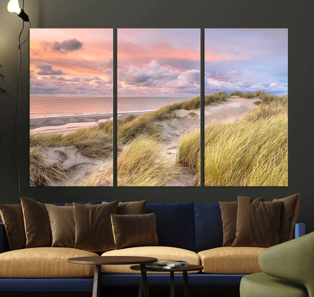 The Ocean Beach Wall Art Canvas Print Sunset Artwork captures a stunning sunset over sand dunes and grass, adding a touch of coastal charm to the room. This piece of wall art infuses any space with warmth and serenity.