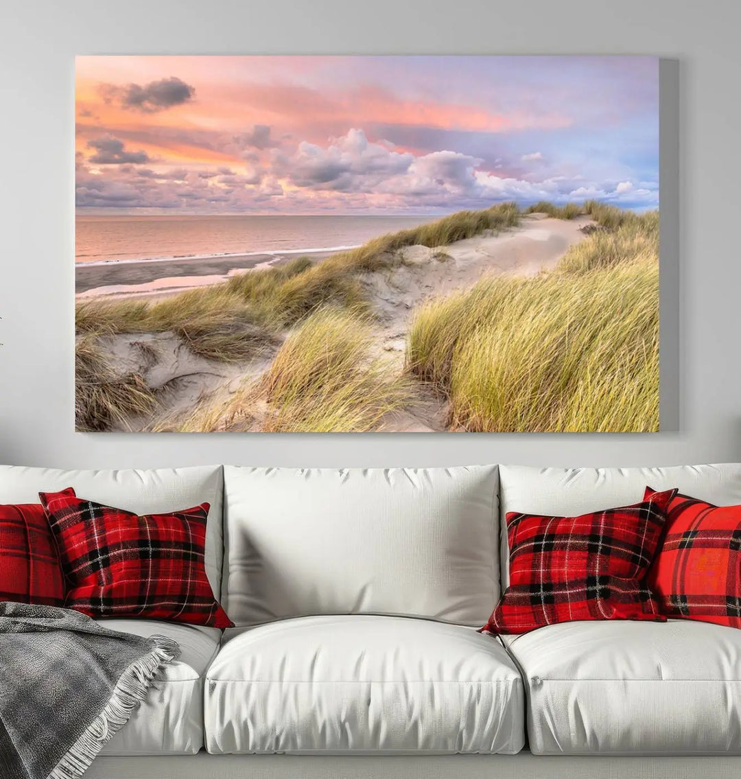 The Ocean Beach Wall Art Canvas Print Sunset Artwork captures a stunning sunset over sand dunes and grass, adding a touch of coastal charm to the room. This piece of wall art infuses any space with warmth and serenity.