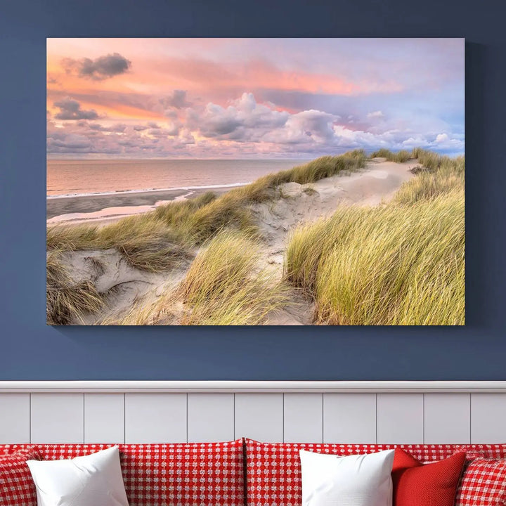 The Ocean Beach Wall Art Canvas Print Sunset Artwork captures a stunning sunset over sand dunes and grass, adding a touch of coastal charm to the room. This piece of wall art infuses any space with warmth and serenity.