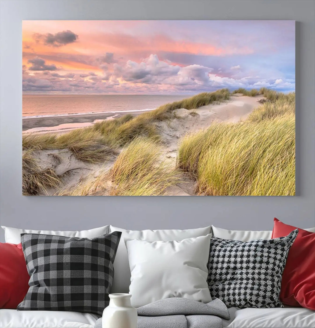 The Ocean Beach Wall Art Canvas Print Sunset Artwork captures a stunning sunset over sand dunes and grass, adding a touch of coastal charm to the room. This piece of wall art infuses any space with warmth and serenity.