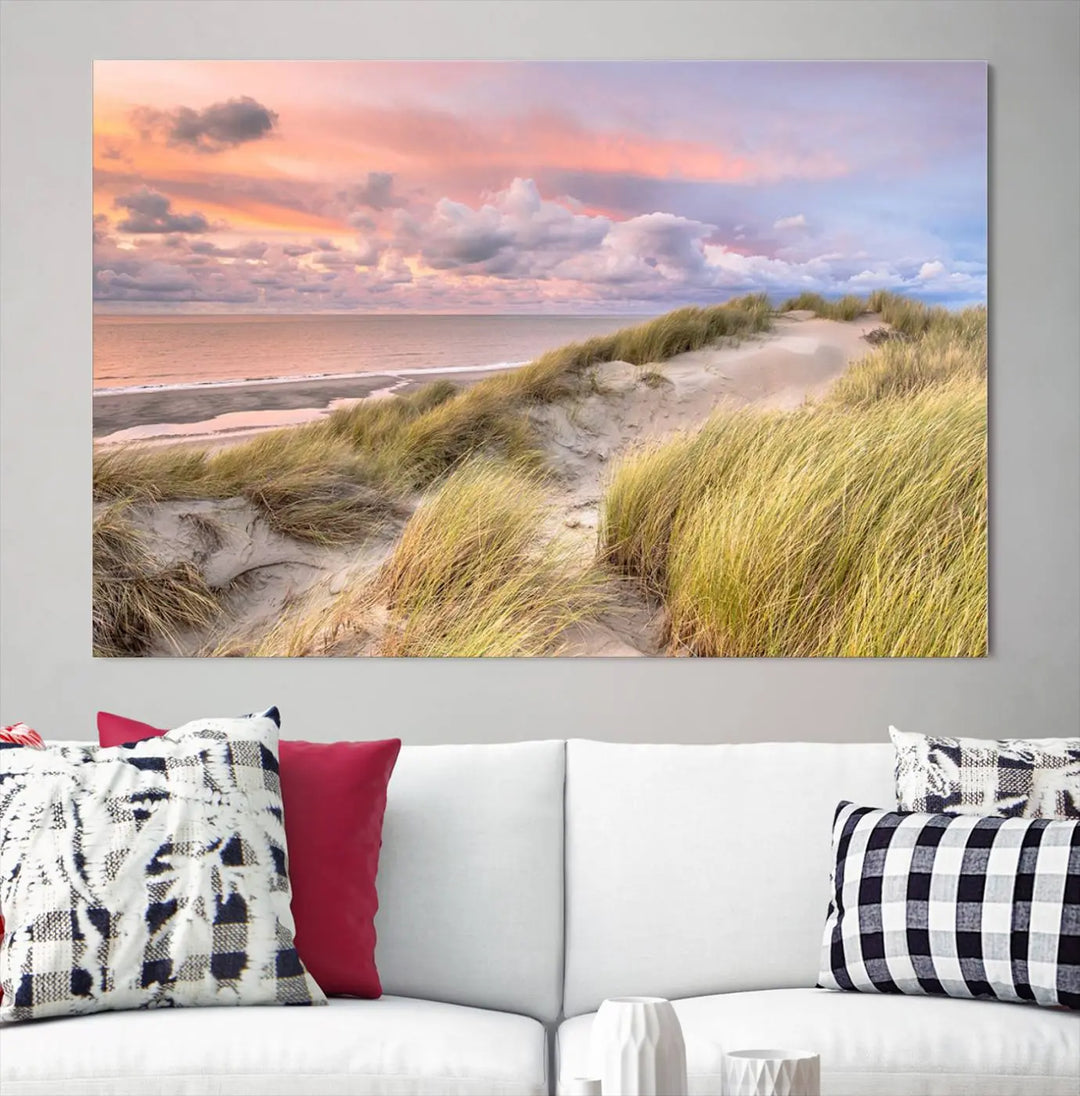 The Ocean Beach Wall Art Canvas Print Sunset Artwork captures a stunning sunset over sand dunes and grass, adding a touch of coastal charm to the room. This piece of wall art infuses any space with warmth and serenity.