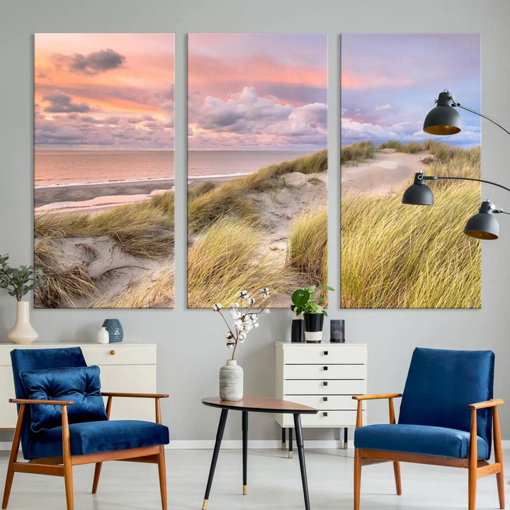 The Ocean Beach Wall Art Canvas Print Sunset Artwork captures a stunning sunset over sand dunes and grass, adding a touch of coastal charm to the room. This piece of wall art infuses any space with warmth and serenity.