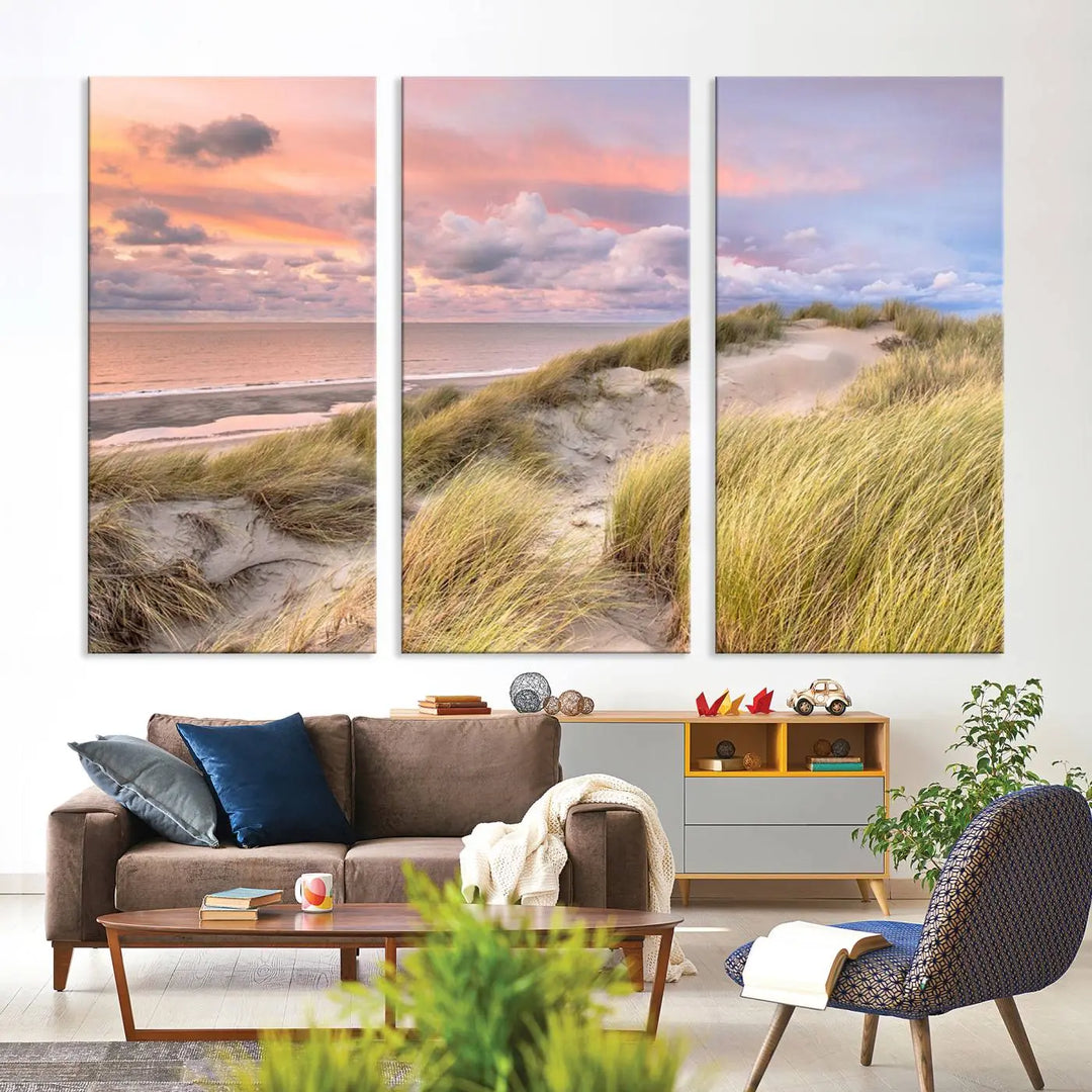 The Ocean Beach Wall Art Canvas Print Sunset Artwork captures a stunning sunset over sand dunes and grass, adding a touch of coastal charm to the room. This piece of wall art infuses any space with warmth and serenity.