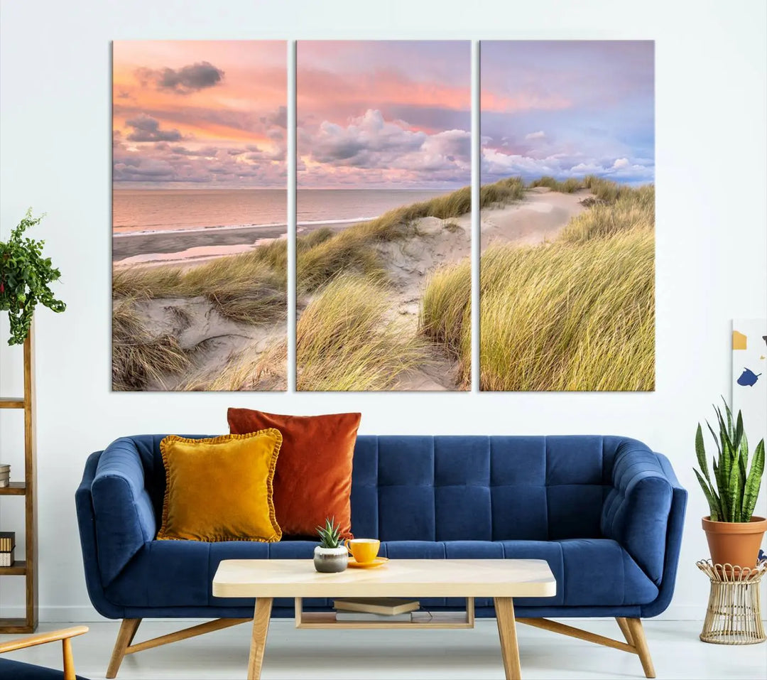 The Ocean Beach Wall Art Canvas Print Sunset Artwork captures a stunning sunset over sand dunes and grass, adding a touch of coastal charm to the room. This piece of wall art infuses any space with warmth and serenity.