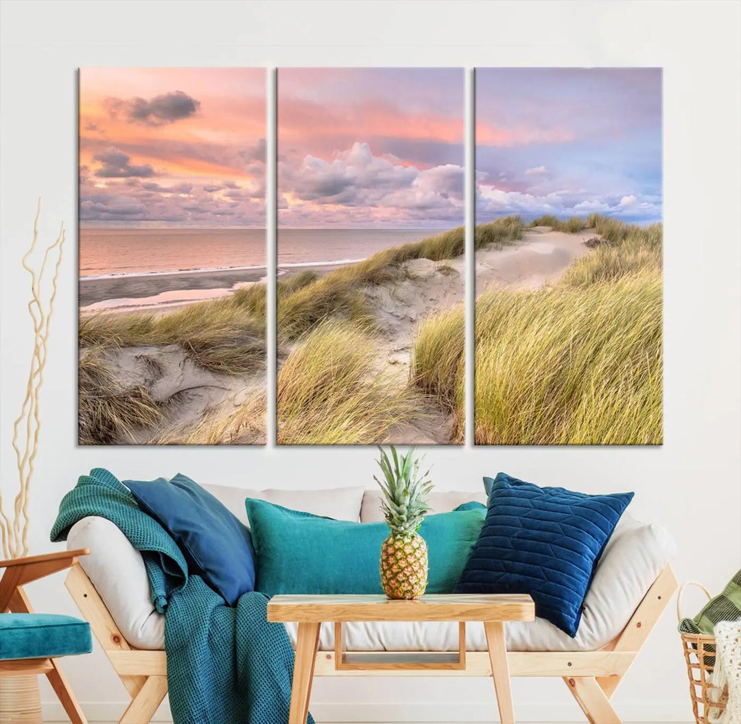 The Ocean Beach Wall Art Canvas Print Sunset Artwork captures a stunning sunset over sand dunes and grass, adding a touch of coastal charm to the room. This piece of wall art infuses any space with warmth and serenity.