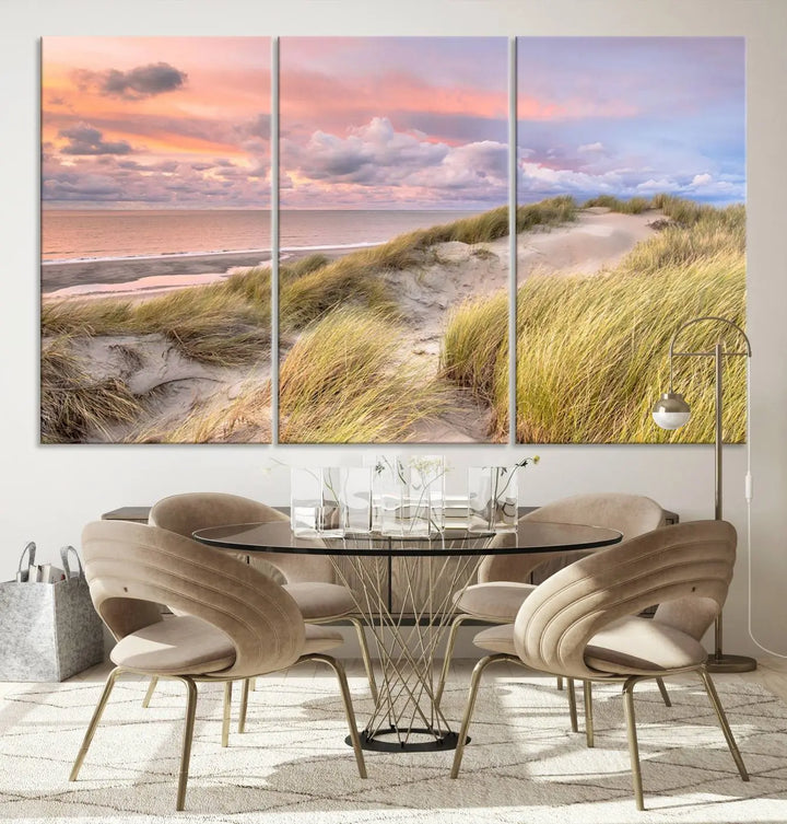 The Ocean Beach Wall Art Canvas Print Sunset Artwork captures a stunning sunset over sand dunes and grass, adding a touch of coastal charm to the room. This piece of wall art infuses any space with warmth and serenity.