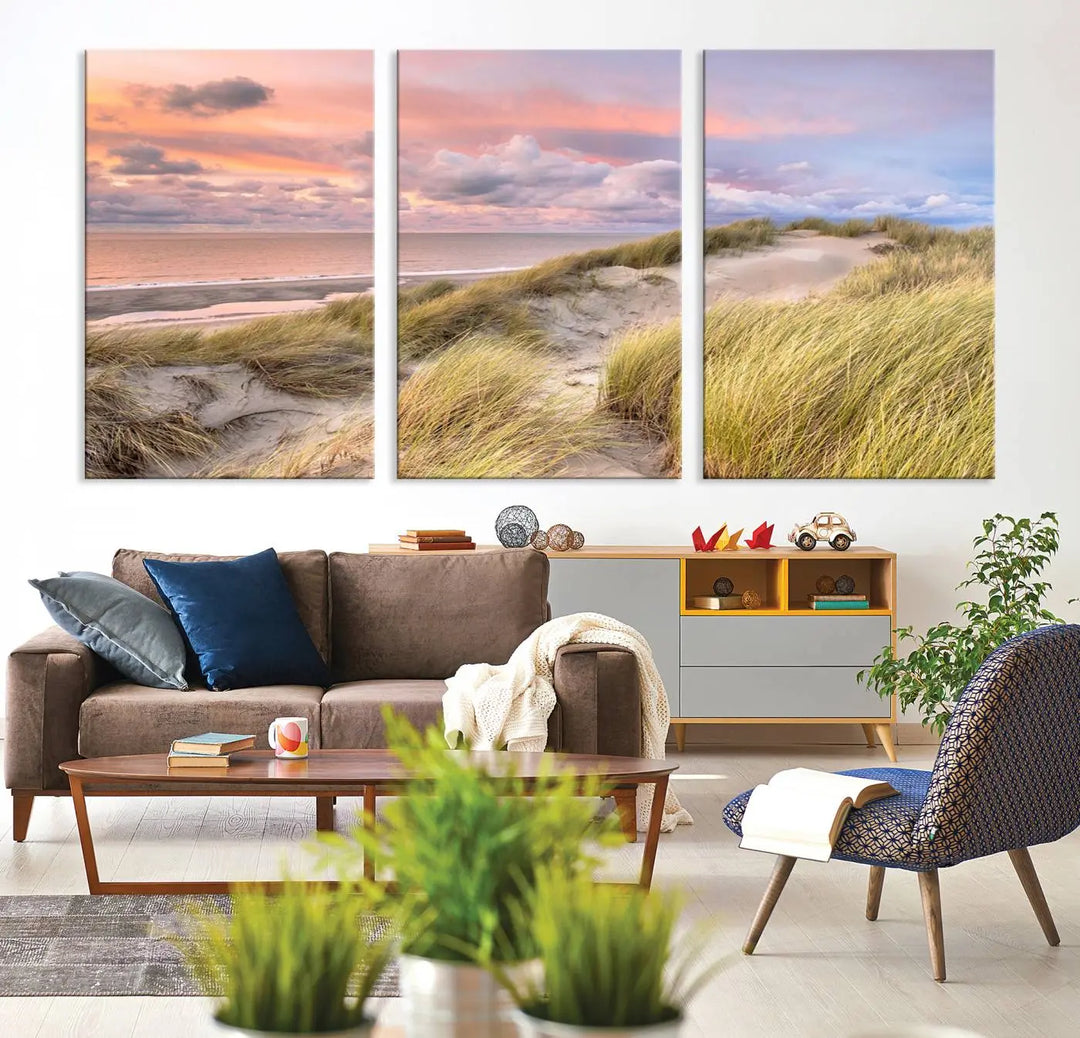 The Ocean Beach Wall Art Canvas Print Sunset Artwork captures a stunning sunset over sand dunes and grass, adding a touch of coastal charm to the room. This piece of wall art infuses any space with warmth and serenity.