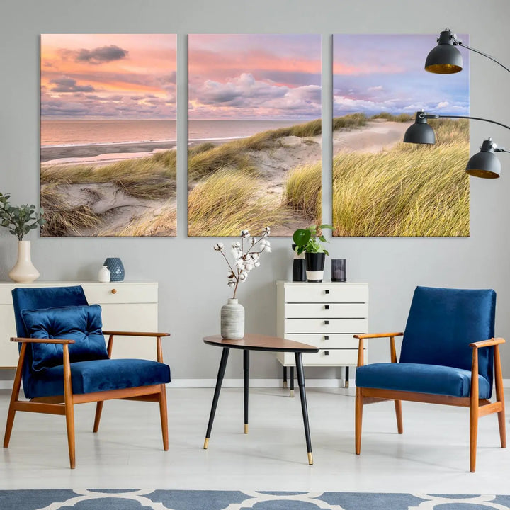 The Ocean Beach Wall Art Canvas Print Sunset Artwork captures a stunning sunset over sand dunes and grass, adding a touch of coastal charm to the room. This piece of wall art infuses any space with warmth and serenity.