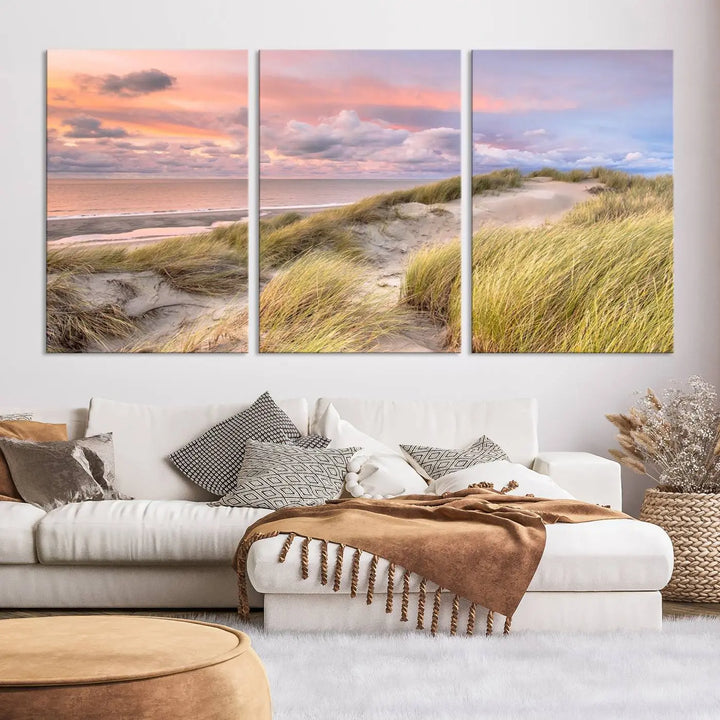 The Ocean Beach Wall Art Canvas Print Sunset Artwork captures a stunning sunset over sand dunes and grass, adding a touch of coastal charm to the room. This piece of wall art infuses any space with warmth and serenity.