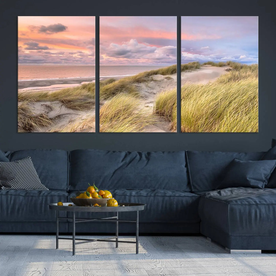 The Ocean Beach Wall Art Canvas Print Sunset Artwork captures a stunning sunset over sand dunes and grass, adding a touch of coastal charm to the room. This piece of wall art infuses any space with warmth and serenity.