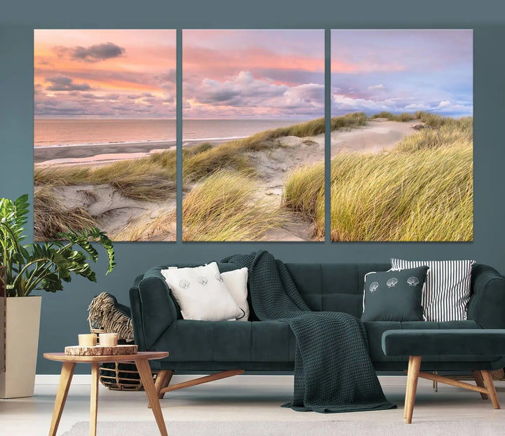 The Ocean Beach Wall Art Canvas Print Sunset Artwork captures a stunning sunset over sand dunes and grass, adding a touch of coastal charm to the room. This piece of wall art infuses any space with warmth and serenity.