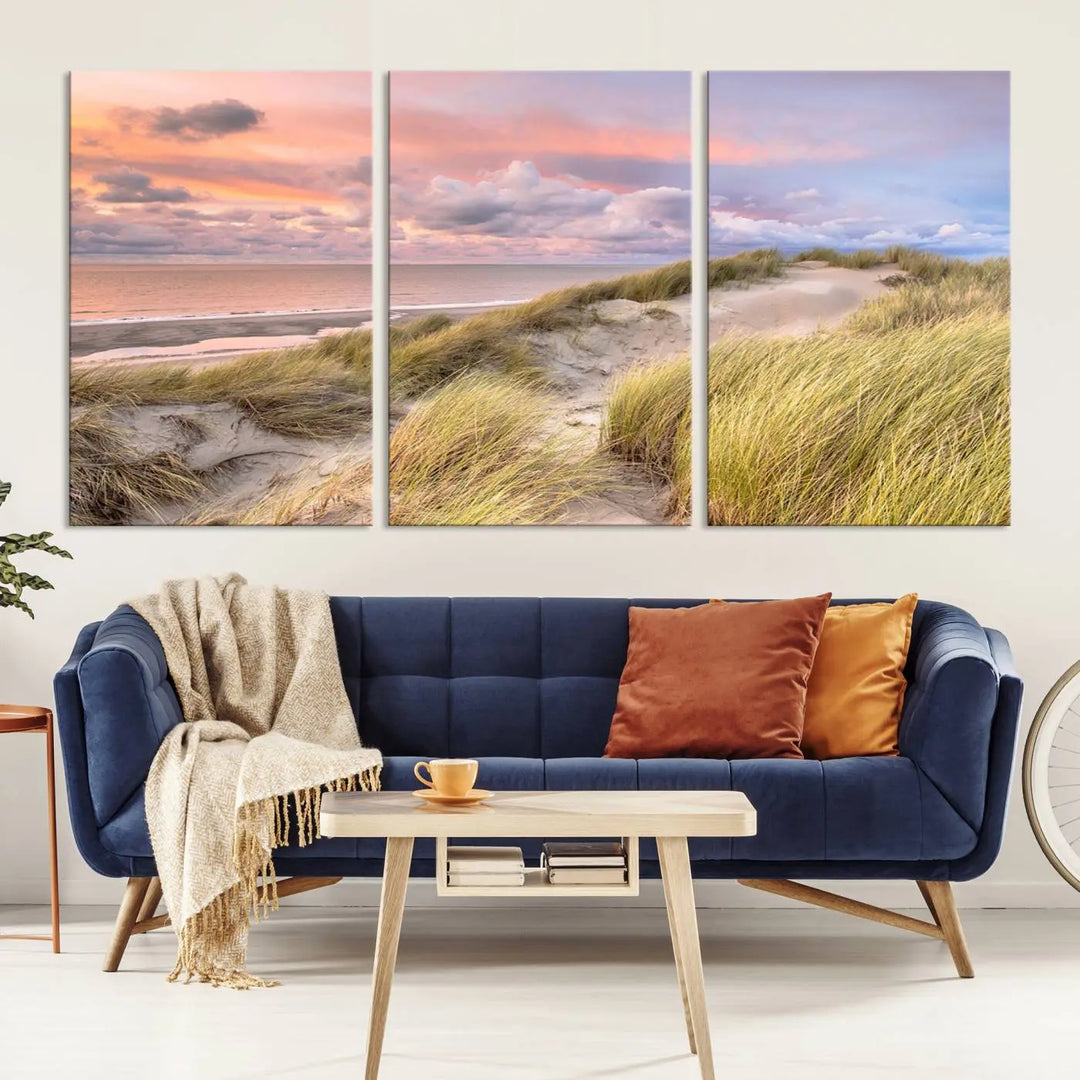 The Ocean Beach Wall Art Canvas Print Sunset Artwork captures a stunning sunset over sand dunes and grass, adding a touch of coastal charm to the room. This piece of wall art infuses any space with warmth and serenity.