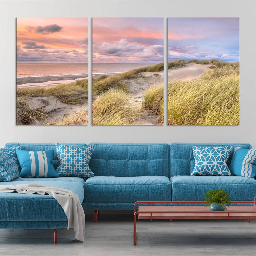 The Ocean Beach Wall Art Canvas Print Sunset Artwork captures a stunning sunset over sand dunes and grass, adding a touch of coastal charm to the room. This piece of wall art infuses any space with warmth and serenity.