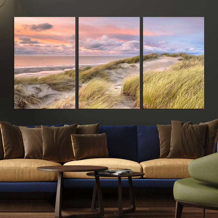 The Ocean Beach Wall Art Canvas Print Sunset Artwork captures a stunning sunset over sand dunes and grass, adding a touch of coastal charm to the room. This piece of wall art infuses any space with warmth and serenity.