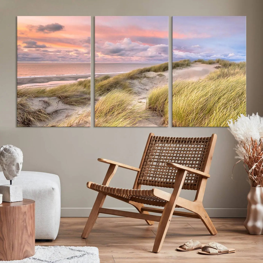 The Ocean Beach Wall Art Canvas Print Sunset Artwork captures a stunning sunset over sand dunes and grass, adding a touch of coastal charm to the room. This piece of wall art infuses any space with warmth and serenity.