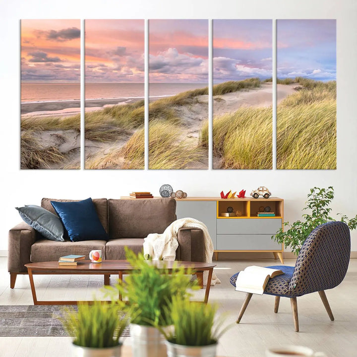 The Ocean Beach Wall Art Canvas Print Sunset Artwork captures a stunning sunset over sand dunes and grass, adding a touch of coastal charm to the room. This piece of wall art infuses any space with warmth and serenity.