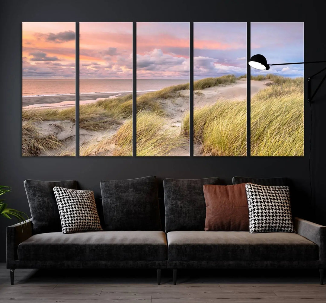 The Ocean Beach Wall Art Canvas Print Sunset Artwork captures a stunning sunset over sand dunes and grass, adding a touch of coastal charm to the room. This piece of wall art infuses any space with warmth and serenity.