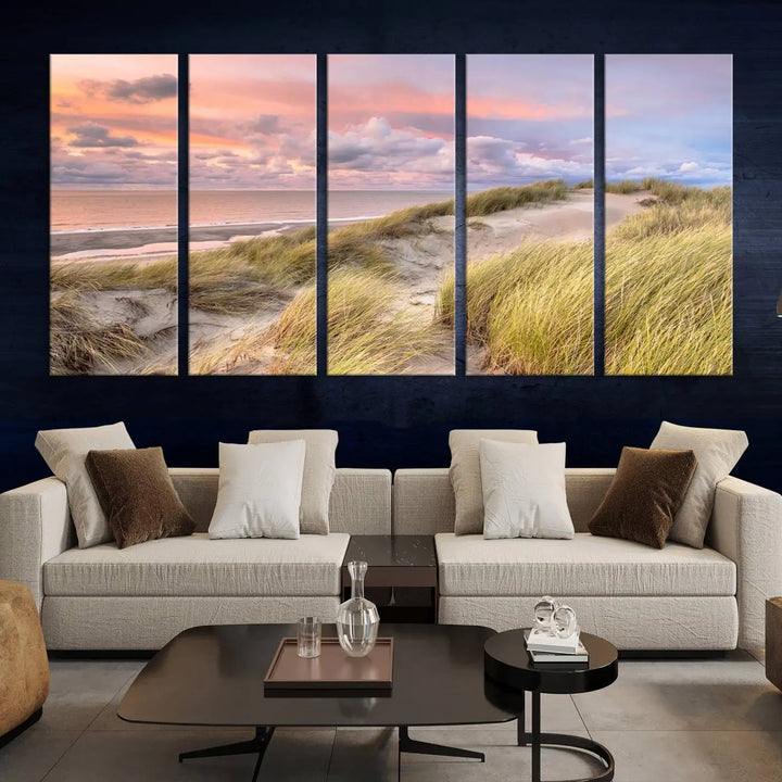 The Ocean Beach Wall Art Canvas Print Sunset Artwork captures a stunning sunset over sand dunes and grass, adding a touch of coastal charm to the room. This piece of wall art infuses any space with warmth and serenity.