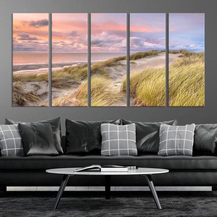 The Ocean Beach Wall Art Canvas Print Sunset Artwork captures a stunning sunset over sand dunes and grass, adding a touch of coastal charm to the room. This piece of wall art infuses any space with warmth and serenity.