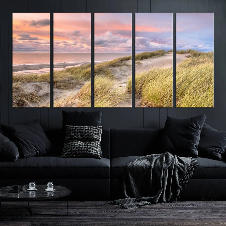 The Ocean Beach Wall Art Canvas Print Sunset Artwork captures a stunning sunset over sand dunes and grass, adding a touch of coastal charm to the room. This piece of wall art infuses any space with warmth and serenity.