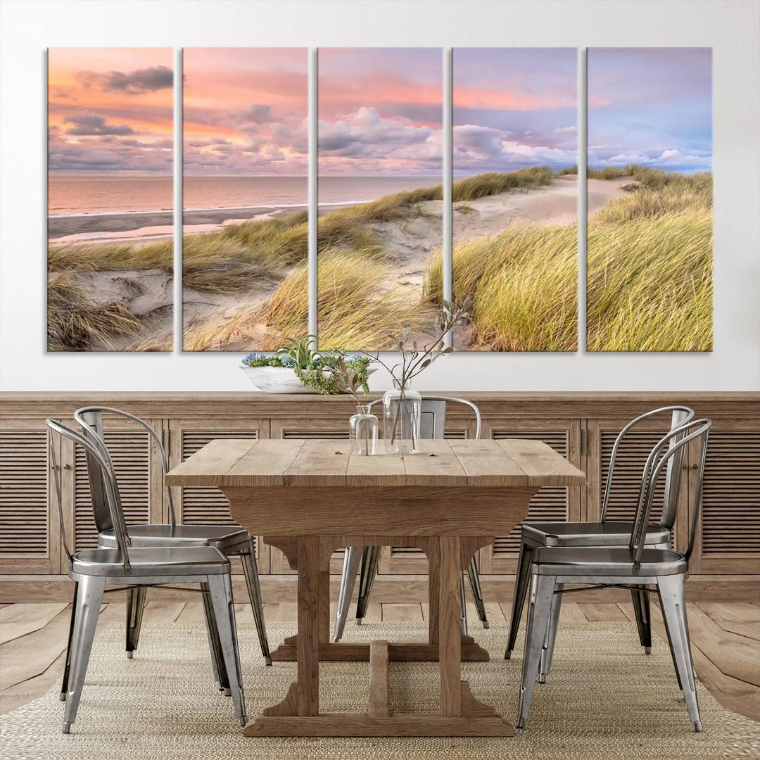 The Ocean Beach Wall Art Canvas Print Sunset Artwork captures a stunning sunset over sand dunes and grass, adding a touch of coastal charm to the room. This piece of wall art infuses any space with warmth and serenity.