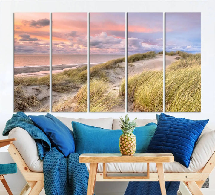 The Ocean Beach Wall Art Canvas Print Sunset Artwork captures a stunning sunset over sand dunes and grass, adding a touch of coastal charm to the room. This piece of wall art infuses any space with warmth and serenity.