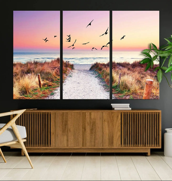 The "Ocean Pathway Sunset Canvas Art" beautifully depicts a tranquil coastal beach walk at sunset, featuring birds in flight across a vividly colorful sky. This piece is crafted using giclee print technology on canvas to ensure vibrant colors and exquisite detail for a relaxing wall art experience.