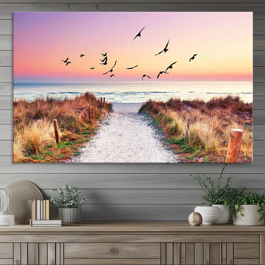 The "Ocean Pathway Sunset Canvas Art" beautifully depicts a tranquil coastal beach walk at sunset, featuring birds in flight across a vividly colorful sky. This piece is crafted using giclee print technology on canvas to ensure vibrant colors and exquisite detail for a relaxing wall art experience.