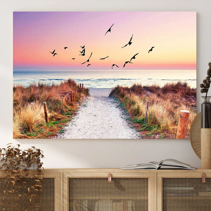 The "Ocean Pathway Sunset Canvas Art" beautifully depicts a tranquil coastal beach walk at sunset, featuring birds in flight across a vividly colorful sky. This piece is crafted using giclee print technology on canvas to ensure vibrant colors and exquisite detail for a relaxing wall art experience.