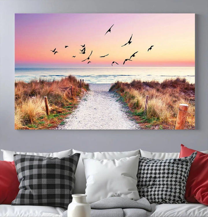 The "Ocean Pathway Sunset Canvas Art" beautifully depicts a tranquil coastal beach walk at sunset, featuring birds in flight across a vividly colorful sky. This piece is crafted using giclee print technology on canvas to ensure vibrant colors and exquisite detail for a relaxing wall art experience.