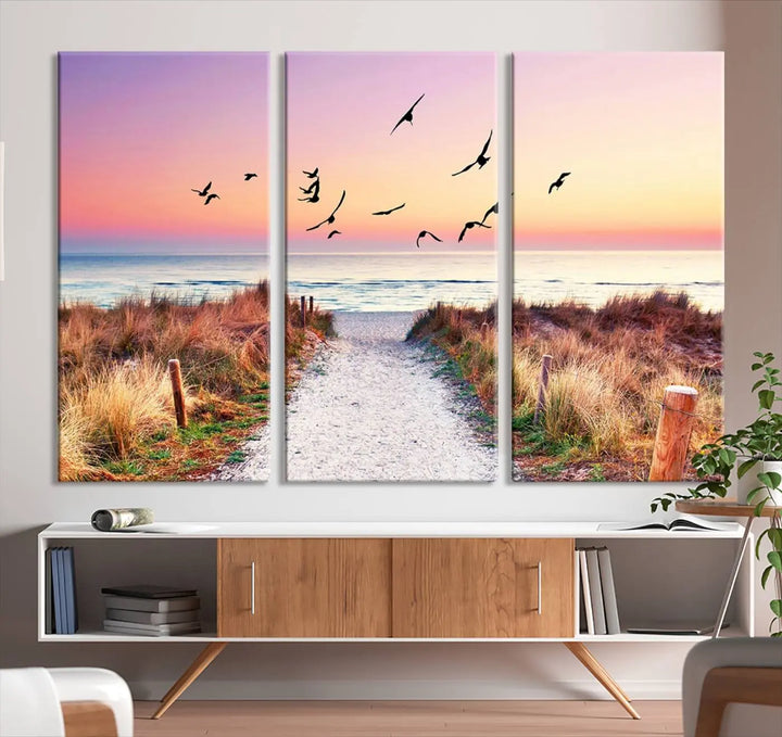 The "Ocean Pathway Sunset Canvas Art" beautifully depicts a tranquil coastal beach walk at sunset, featuring birds in flight across a vividly colorful sky. This piece is crafted using giclee print technology on canvas to ensure vibrant colors and exquisite detail for a relaxing wall art experience.