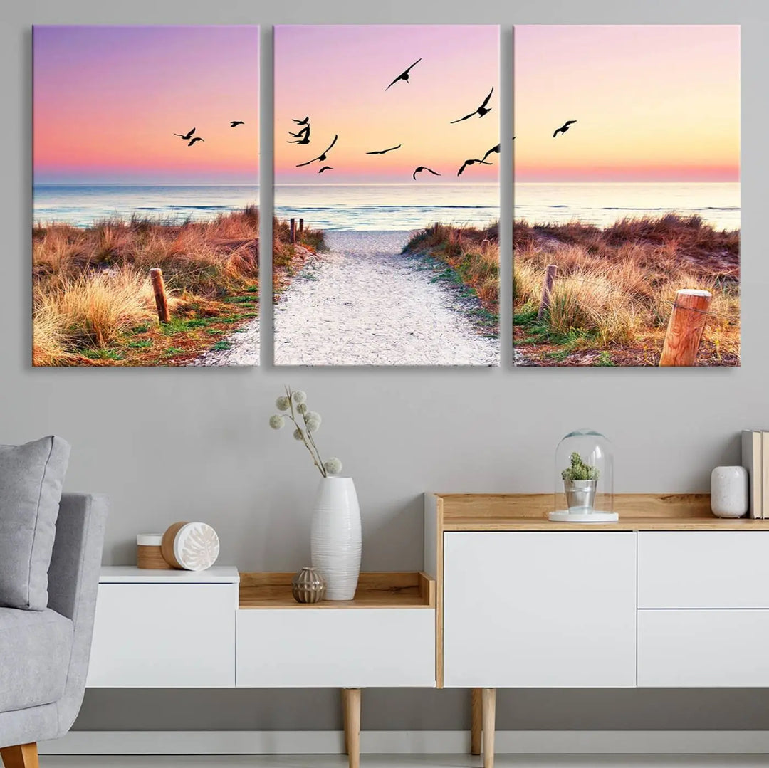 The "Ocean Pathway Sunset Canvas Art" beautifully depicts a tranquil coastal beach walk at sunset, featuring birds in flight across a vividly colorful sky. This piece is crafted using giclee print technology on canvas to ensure vibrant colors and exquisite detail for a relaxing wall art experience.