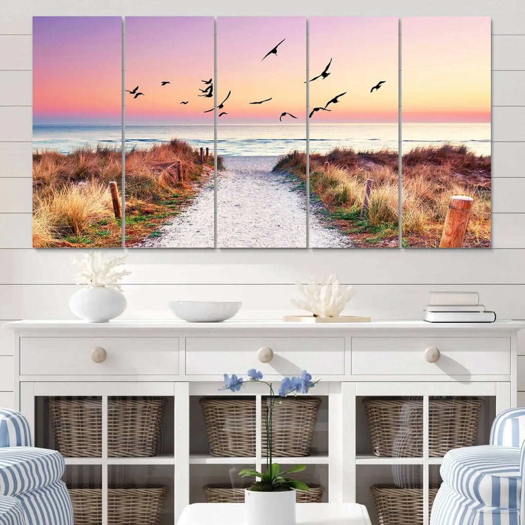 The "Ocean Pathway Sunset Canvas Art" beautifully depicts a tranquil coastal beach walk at sunset, featuring birds in flight across a vividly colorful sky. This piece is crafted using giclee print technology on canvas to ensure vibrant colors and exquisite detail for a relaxing wall art experience.