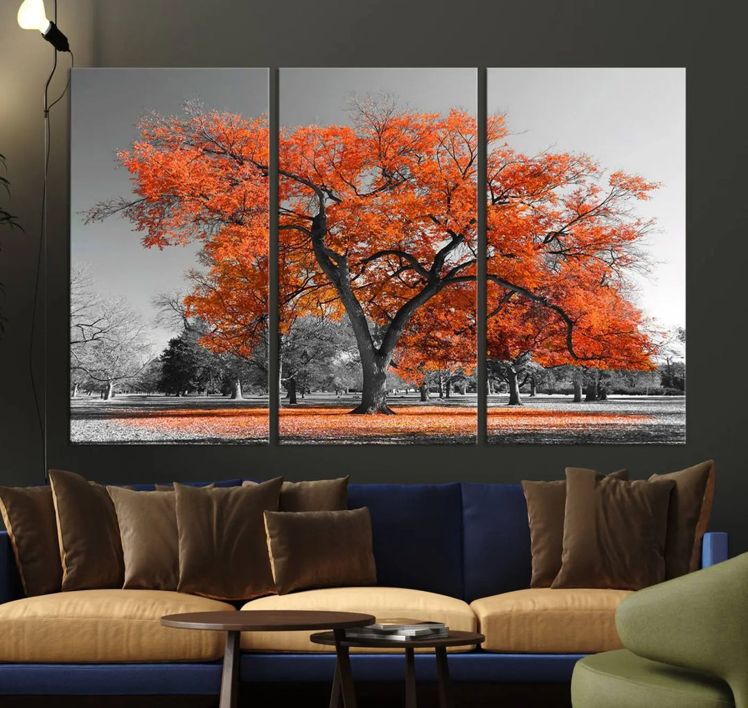 The "Orange Autumn Tree Canvas Wall Art Print" features a triptych of a tree with vibrant orange leaves set in a grayscale park. It's printed on museum-quality canvas and safeguarded by a UV-protective coating, making it the perfect artwork for any space.