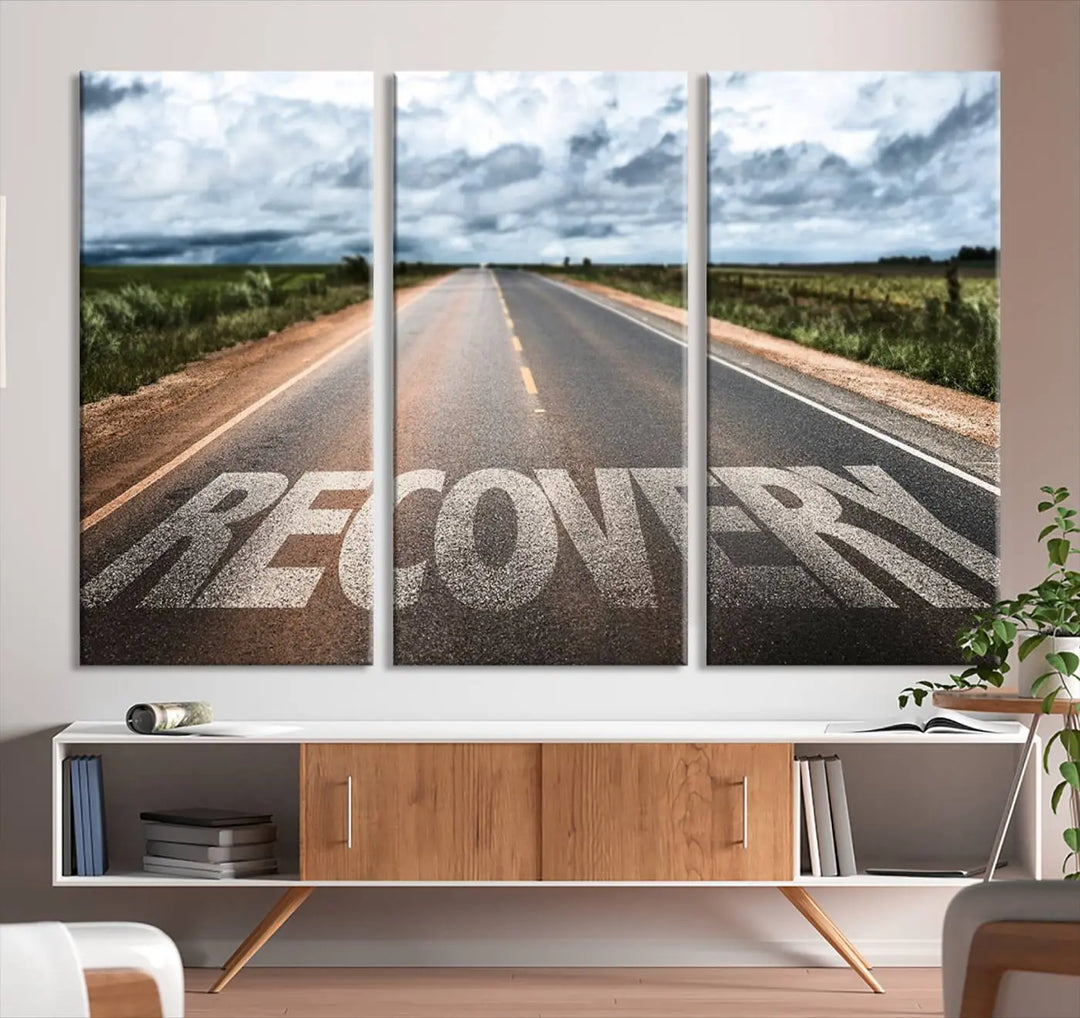 The Recovery Road Wall Art Canvas Print, a three-panel piece gallery wrapped on museum-quality canvas, displays an empty road with the word RECOVERY painted on it. This artwork is coated with UV-protection to maintain its vibrant colors over time.