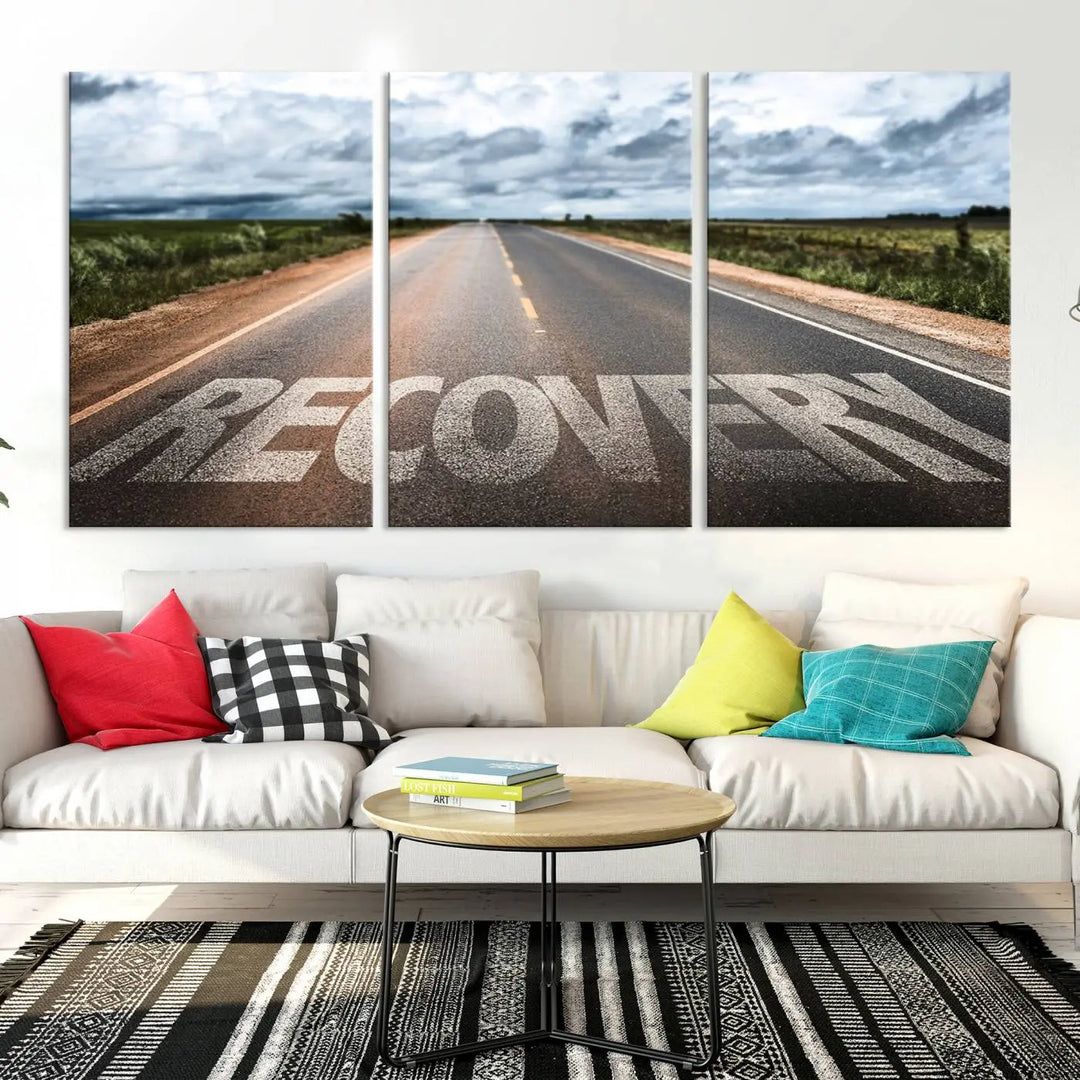 The Recovery Road Wall Art Canvas Print, a three-panel piece gallery wrapped on museum-quality canvas, displays an empty road with the word RECOVERY painted on it. This artwork is coated with UV-protection to maintain its vibrant colors over time.