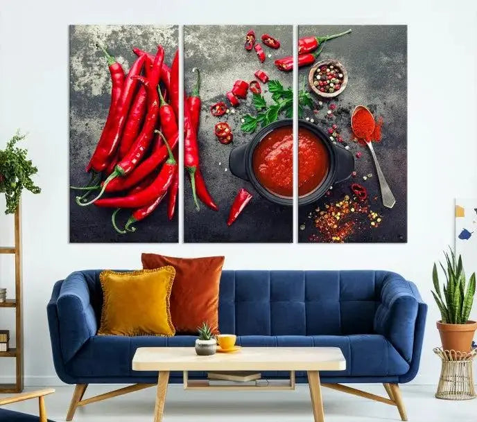 The Red Chili Peppers Wall Art Kitchen Artwork Canvas Print is a three-panel canvas showcasing red chili peppers, sliced chili, a pot of red sauce, and assorted spices on a dark background. It is of museum quality with a UV-protective coating to ensure its colors remain vibrant over time.