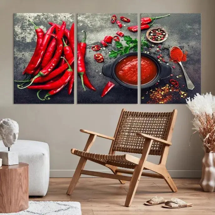 The Red Chili Peppers Wall Art Kitchen Artwork Canvas Print is a three-panel canvas showcasing red chili peppers, sliced chili, a pot of red sauce, and assorted spices on a dark background. It is of museum quality with a UV-protective coating to ensure its colors remain vibrant over time.