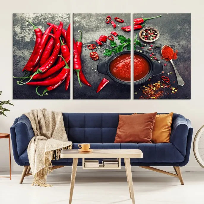 The Red Chili Peppers Wall Art Kitchen Artwork Canvas Print is a three-panel canvas showcasing red chili peppers, sliced chili, a pot of red sauce, and assorted spices on a dark background. It is of museum quality with a UV-protective coating to ensure its colors remain vibrant over time.