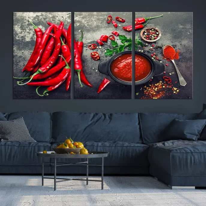 The Red Chili Peppers Wall Art Kitchen Artwork Canvas Print is a three-panel canvas showcasing red chili peppers, sliced chili, a pot of red sauce, and assorted spices on a dark background. It is of museum quality with a UV-protective coating to ensure its colors remain vibrant over time.