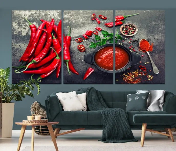 The Red Chili Peppers Wall Art Kitchen Artwork Canvas Print is a three-panel canvas showcasing red chili peppers, sliced chili, a pot of red sauce, and assorted spices on a dark background. It is of museum quality with a UV-protective coating to ensure its colors remain vibrant over time.