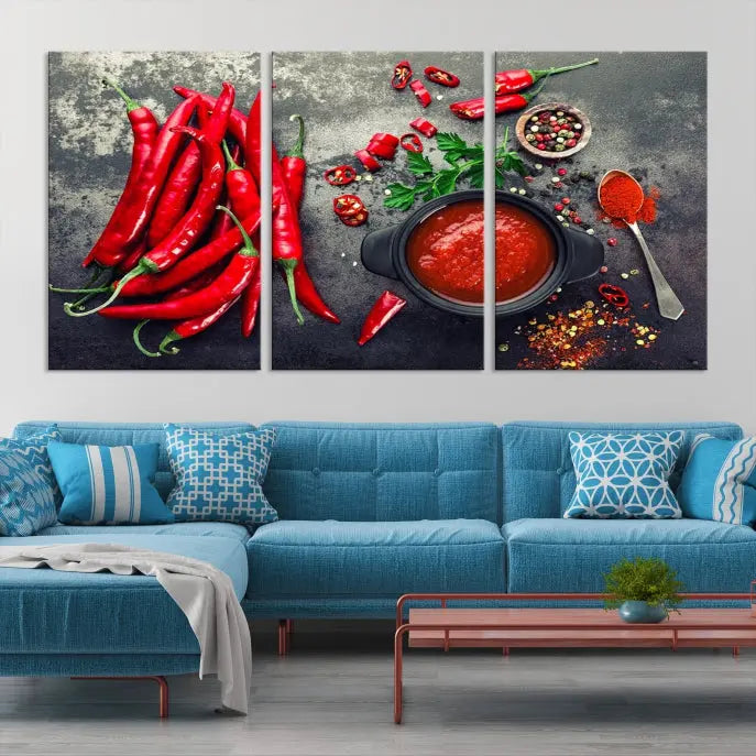 The Red Chili Peppers Wall Art Kitchen Artwork Canvas Print is a three-panel canvas showcasing red chili peppers, sliced chili, a pot of red sauce, and assorted spices on a dark background. It is of museum quality with a UV-protective coating to ensure its colors remain vibrant over time.