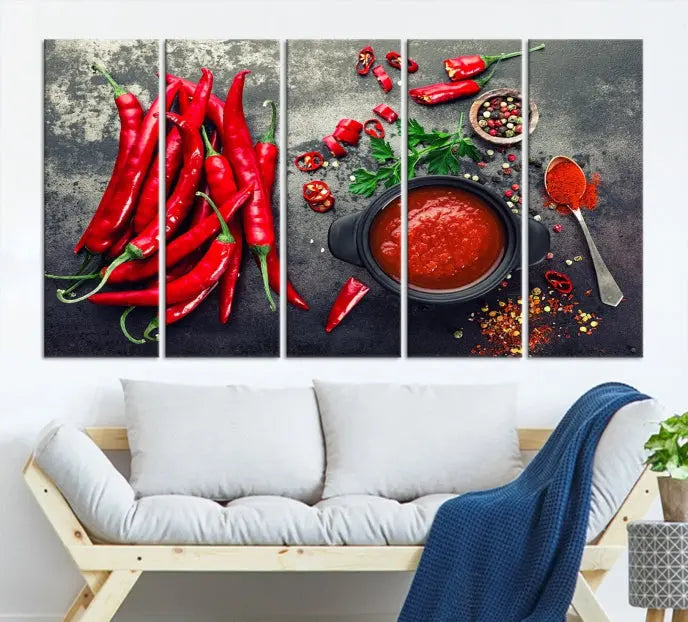 The Red Chili Peppers Wall Art Kitchen Artwork Canvas Print is a three-panel canvas showcasing red chili peppers, sliced chili, a pot of red sauce, and assorted spices on a dark background. It is of museum quality with a UV-protective coating to ensure its colors remain vibrant over time.