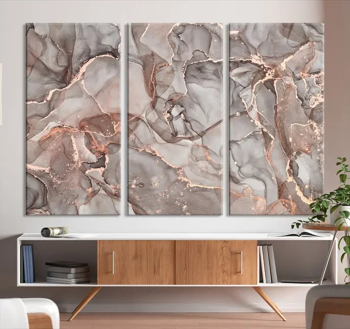 The Rose Gold Marble Fluid Effect Wall Art Abstract Canvas Wall Art Print is an exquisite three-panel creation crafted on museum-quality canvas. It features swirling marbled patterns in shades of gray, copper, and beige. Complete with a UV-protective coating, this ready-to-hang artwork promises to be a timeless addition to any space.