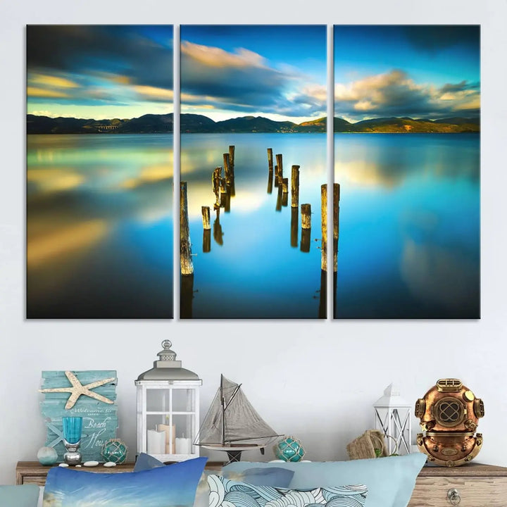 A triptych of a serene lake scene with old wooden pillars, blue sky, and clouds casts a coastal ambiance. The Sea Ocean Sunset Beach Wall Art Canvas Print reflects the soothing nature of the ocean.