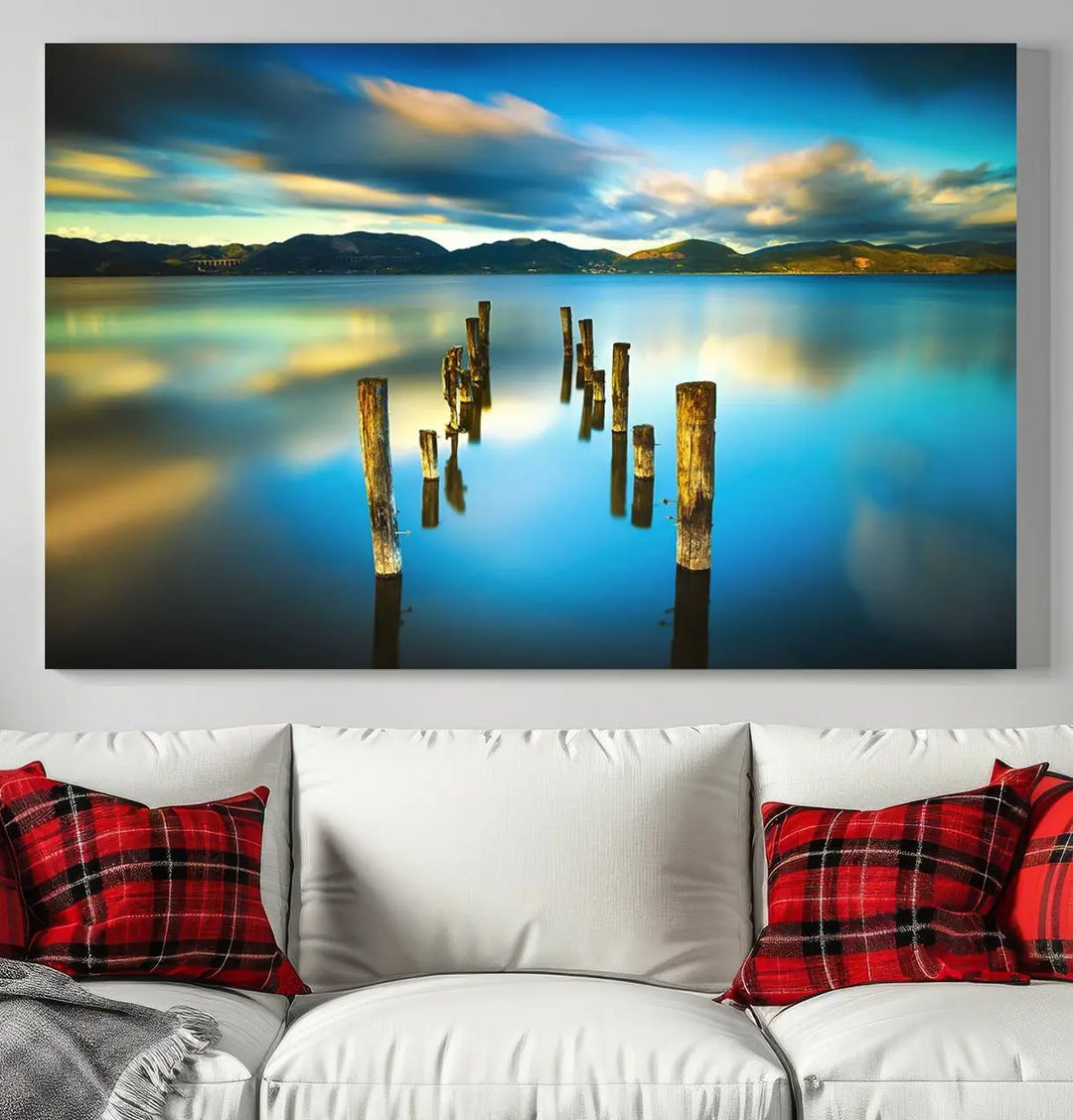 A triptych of a serene lake scene with old wooden pillars, blue sky, and clouds casts a coastal ambiance. The Sea Ocean Sunset Beach Wall Art Canvas Print reflects the soothing nature of the ocean.