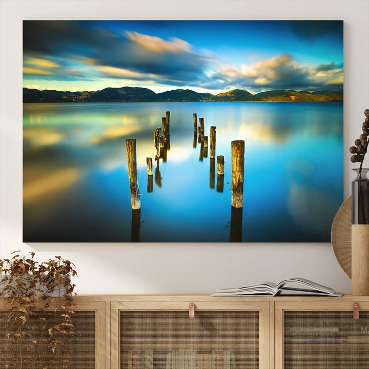 A triptych of a serene lake scene with old wooden pillars, blue sky, and clouds casts a coastal ambiance. The Sea Ocean Sunset Beach Wall Art Canvas Print reflects the soothing nature of the ocean.